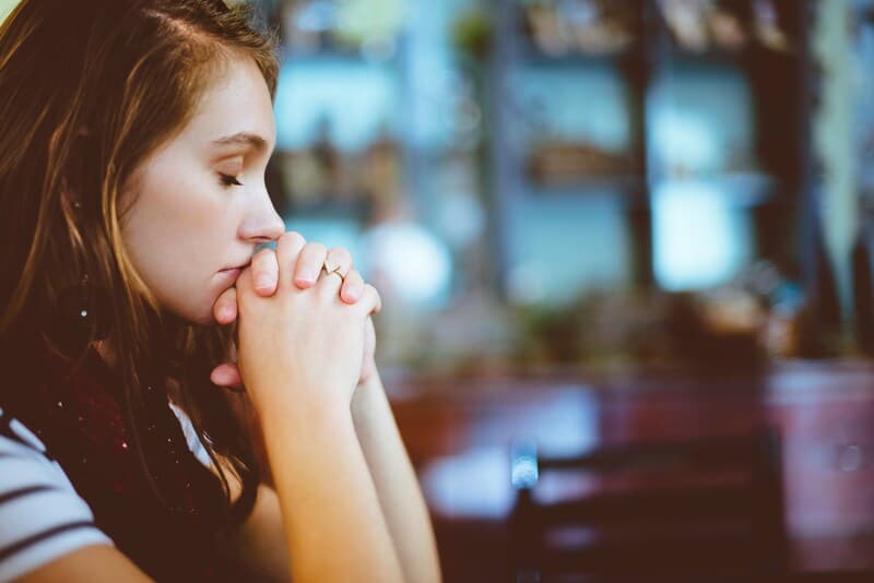 Una joven con los ojos cerrados y las manos juntas en oración, expresando calma y concentración, simbolizando la práctica de empezar cada mes con gratitud.